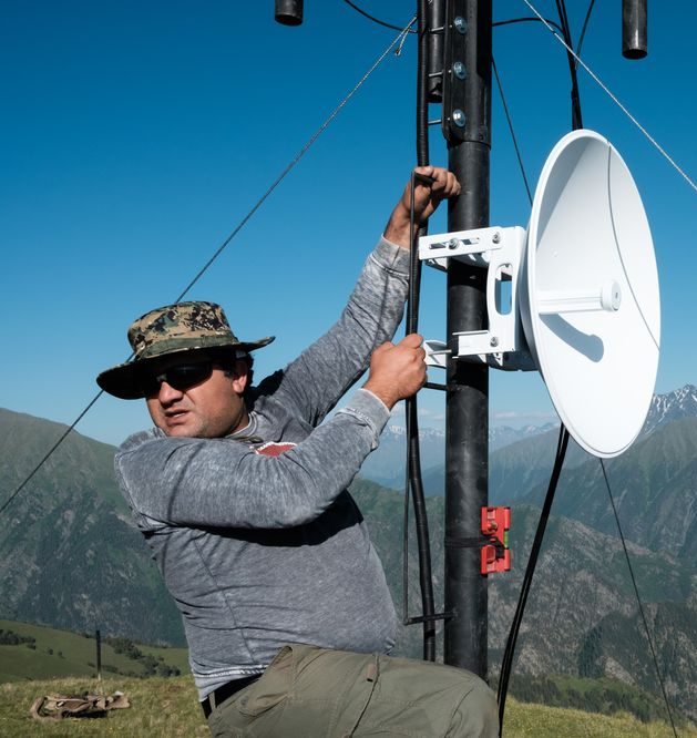 A man climbing on a tower adjusting equipment. He is in Tusheti.