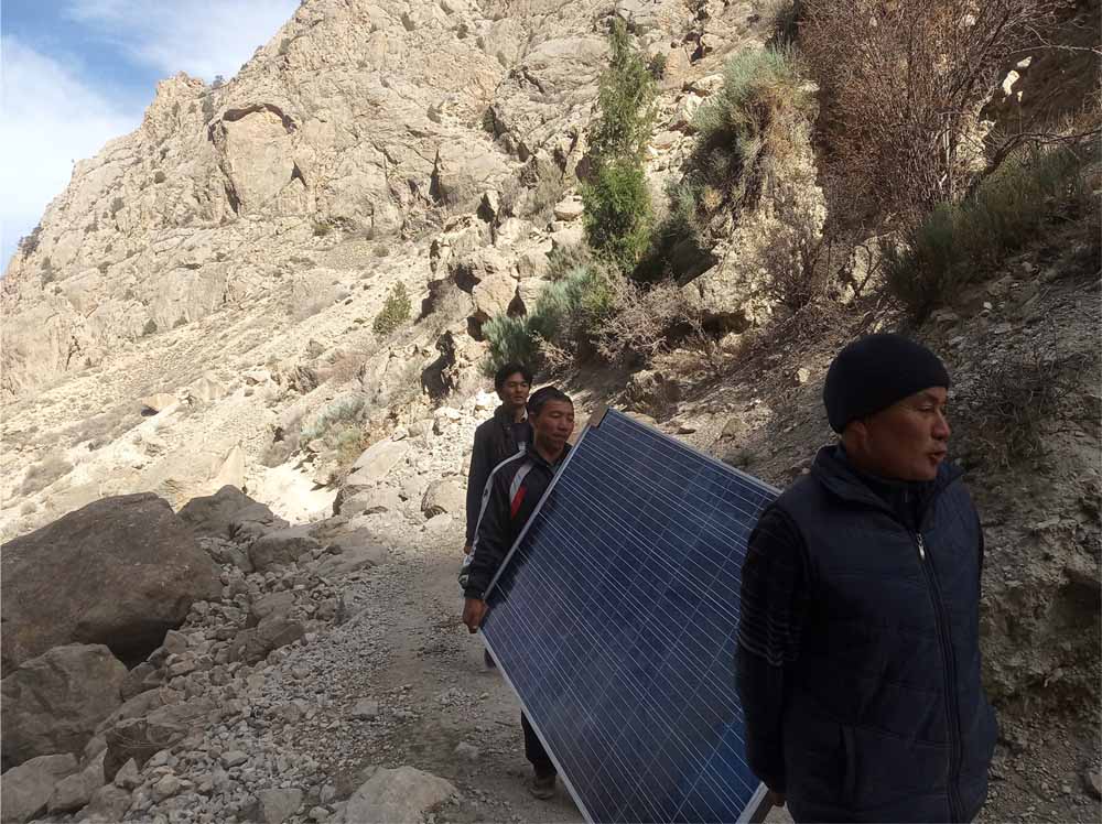 Dos personas transportando un panel solar por un sendero