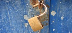 a rusted padlock is open and hanging from a latch. the background looks like blue metal