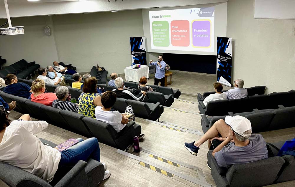 A man stands and speaks to a class with a powerpoint behind him. 