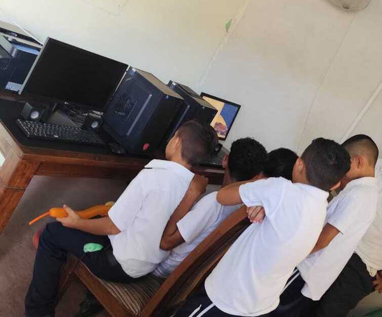 A group of young boys huddles around a computer