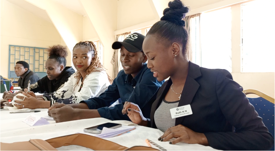 Ruth Njeri sits at a table with several other people and looks at papers. 