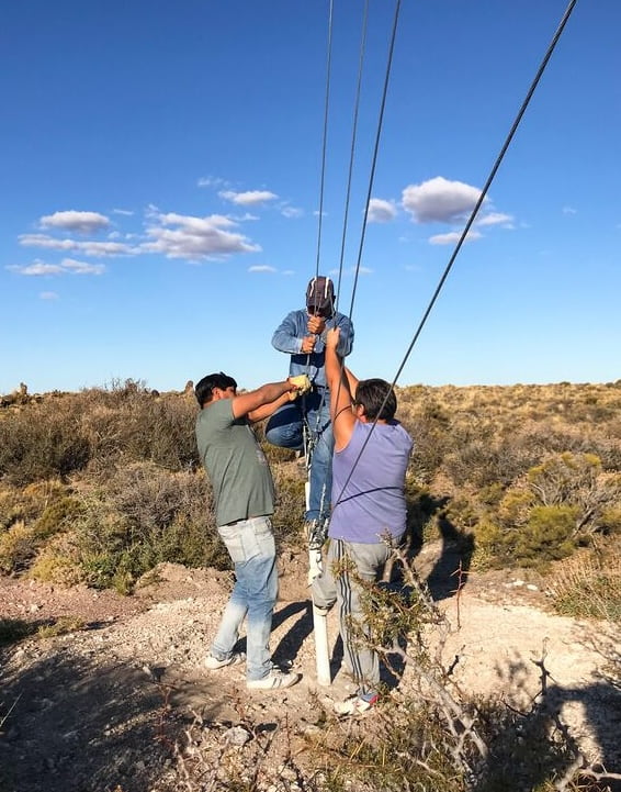 Three men are collaborating on a pole installation in a vast desert landscape