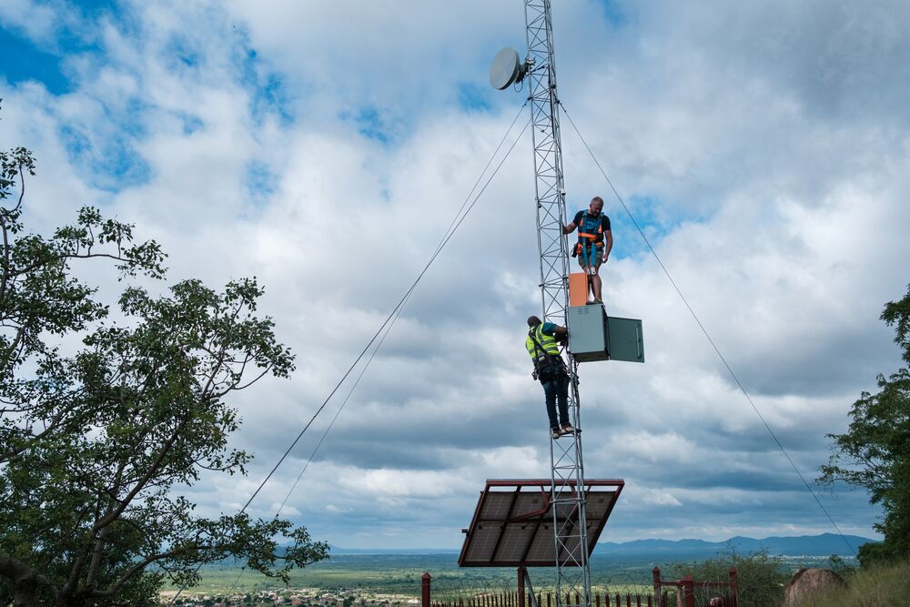 Two men collaborating on a tower against a backdrop of a clear blue sky