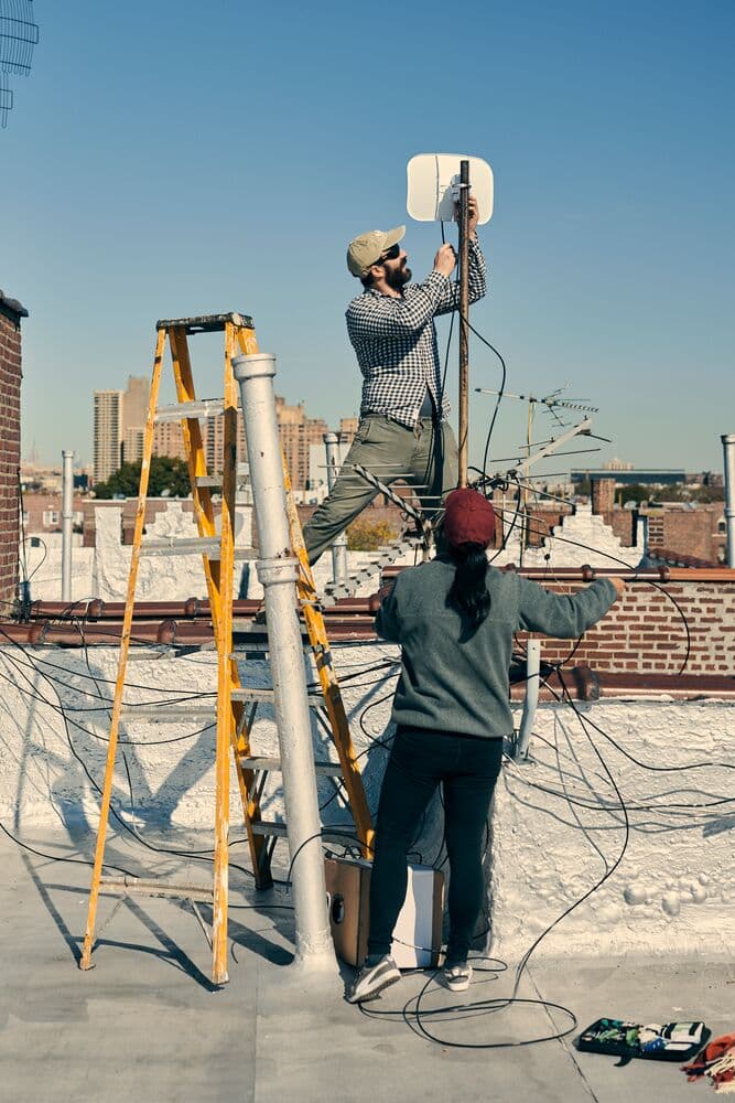 Two people collaborating on a rooftop, utilizing a ladder for their work tasks.